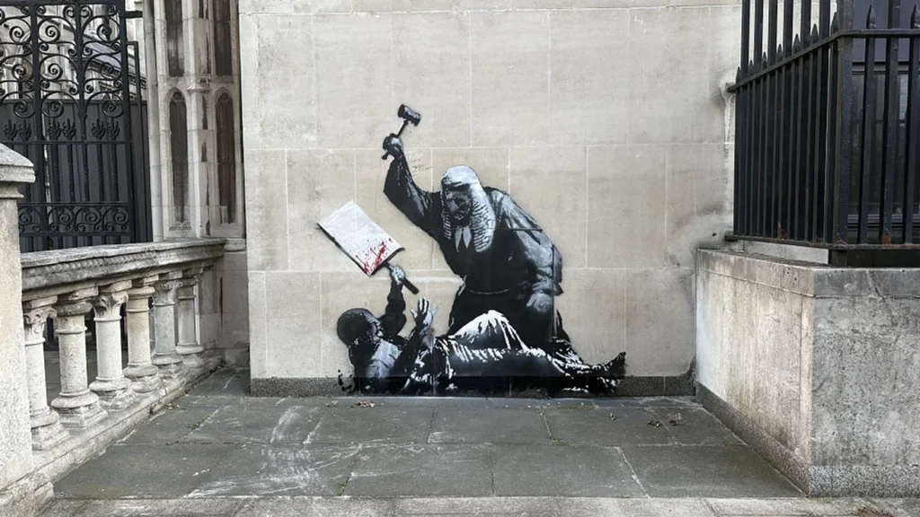 Die Londoner Polizei ermittelt gegen Banksy, nachdem ein neues Graffiti am Royal Courts of Justice aufgetaucht ist. Es geht auch um die Identität des Künstlers.
